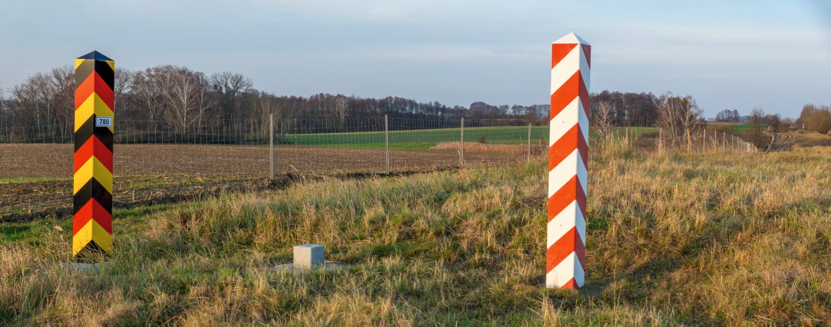Ein Zaun in der Landschaft. Zwei Grenzpfosten mit den Nationalfarben von Polen und Deutschland