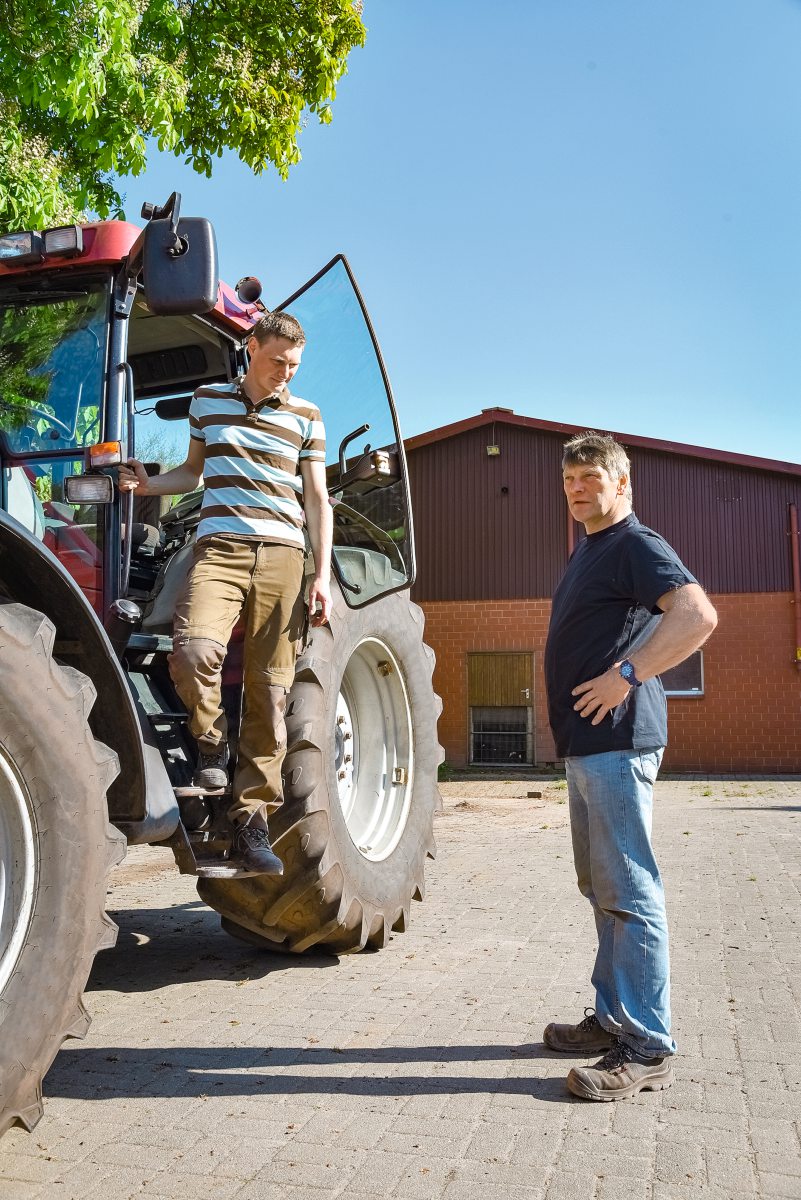 Junger Mann steigt zum Gespräch aus dem Traktor zu einem älterer Mann.