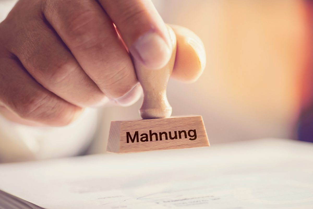 Hand hält einen Stempel mit dem Wort "Mahnung"