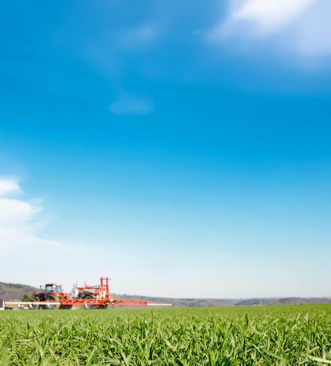 Traktor mit Pflanzenschutzspritze fährt über das Feld
