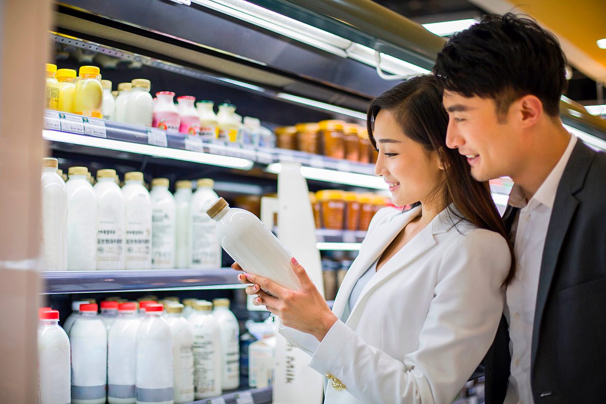 Eine Frau und ein Mann stehen vor einem Regal mit Milch und halten eine Flasche in der Hand