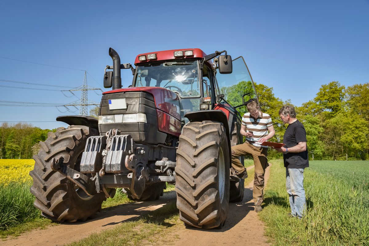 Zwei Männer stehen neben einem Traktor und besprechen sich.