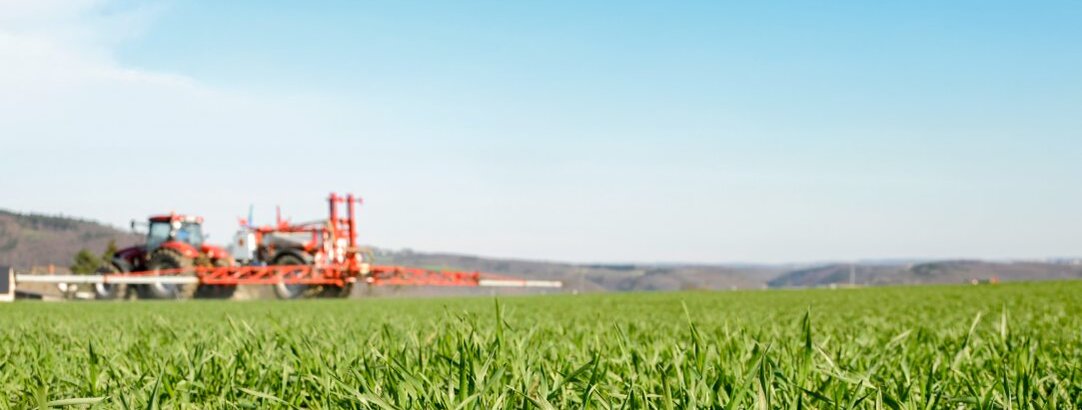 Traktor mit Pflanzenschutzspritze fährt über das Feld