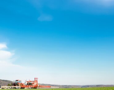 Traktor mit Pflanzenschutzspritze fährt über das Feld