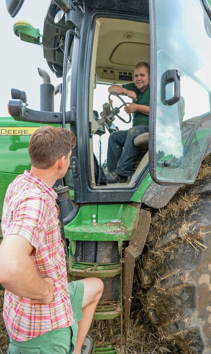 Zwei Landwirte unterhalten sich, einer sitzt auf einem Traktor