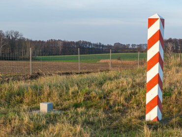 Ein Zaun in der Landschaft. Zwei Grenzpfosten mit den Nationalfarben von Polen und Deutschland