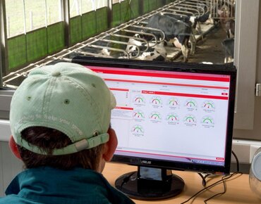Landwirt sitzt im Stallbüro und prüft Daten des Melkroboters
