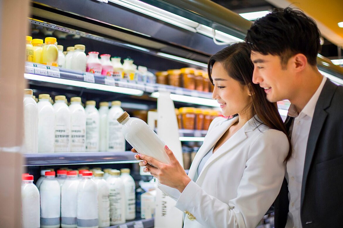 Eine Frau und ein Mann stehen vor einem Regal mit Milch und halten eine Flasche in der Hand