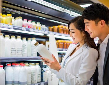 Eine Frau und ein Mann stehen vor einem Regal mit Milch und halten eine Flasche in der Hand
