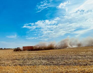 Traktor mit Anhänger fährt über ein Feld, extreme Staubentwicklung wegen Trockenheit