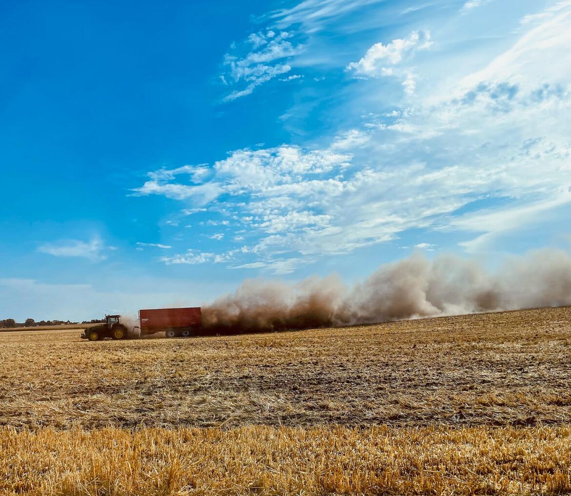 Traktor mit Anhänger fährt über ein Feld, extreme Staubentwicklung wegen Trockenheit