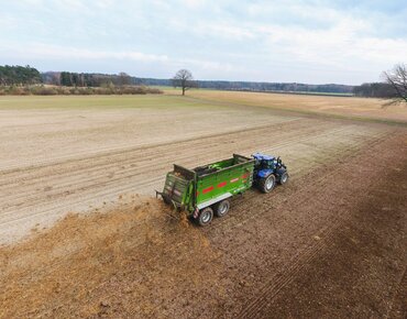 Traktor mit einem Festmiststreuer fährt über ein Stoppelfeld