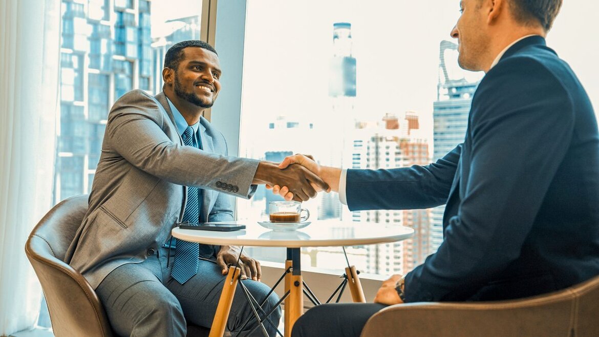 Zwei Männer sitzen an einem Tisch und geben sich die Hand