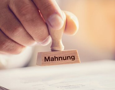 Hand hält einen Stempel mit dem Wort "Mahnung"