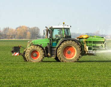 Traktor mit Düngerstreuer fährt über ein Feld