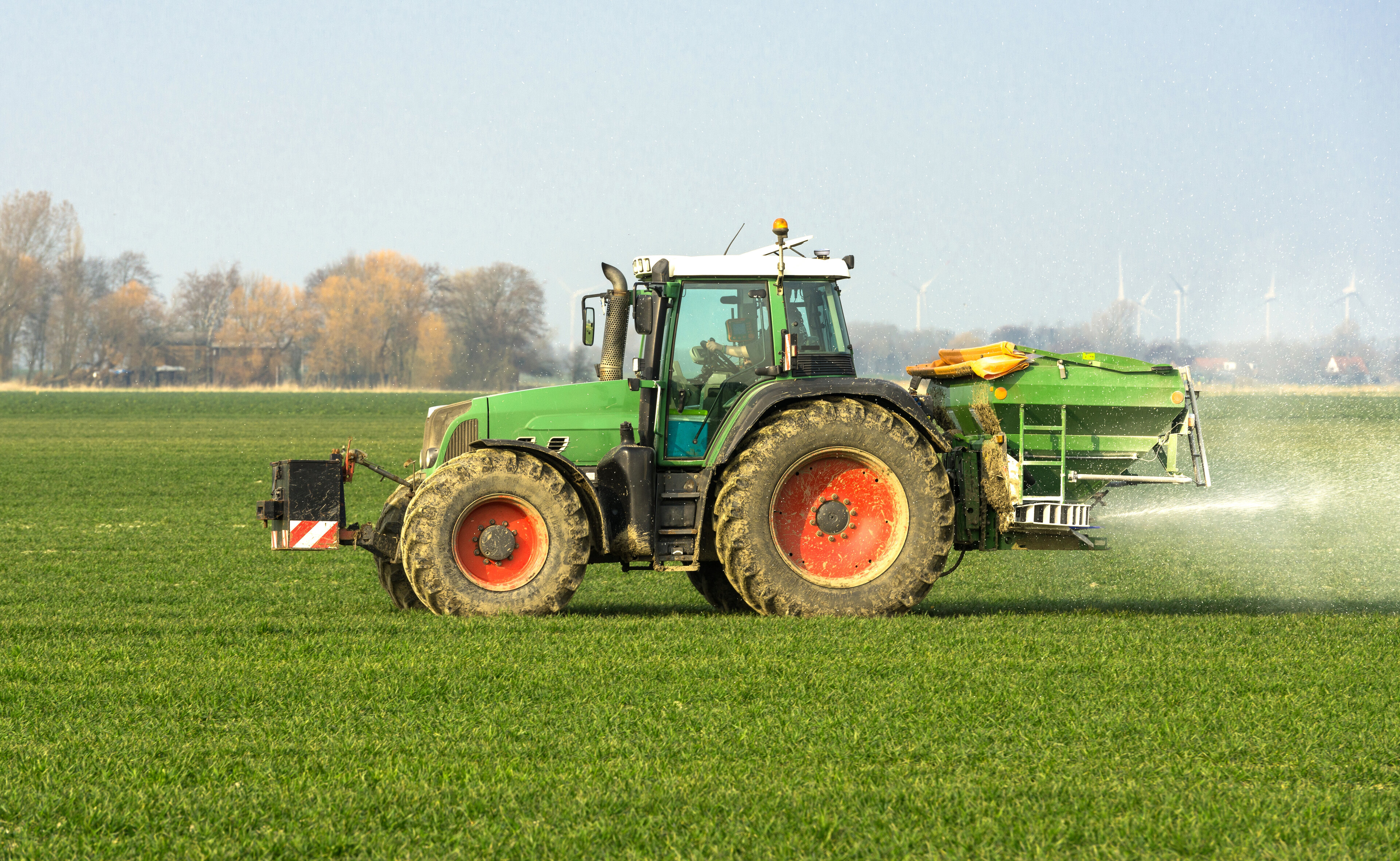 Traktor mit Düngerstreuer fährt über ein Feld