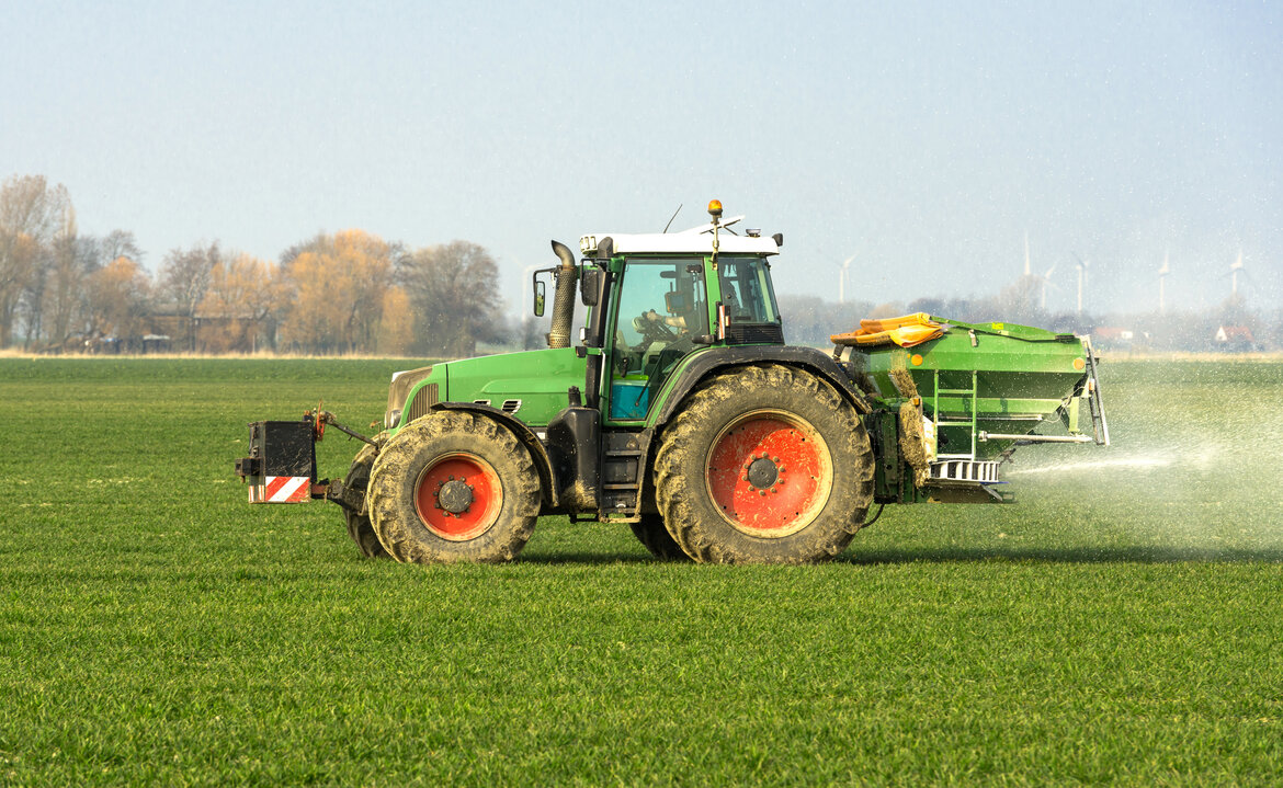 Traktor mit Düngerstreuer fährt über ein Feld