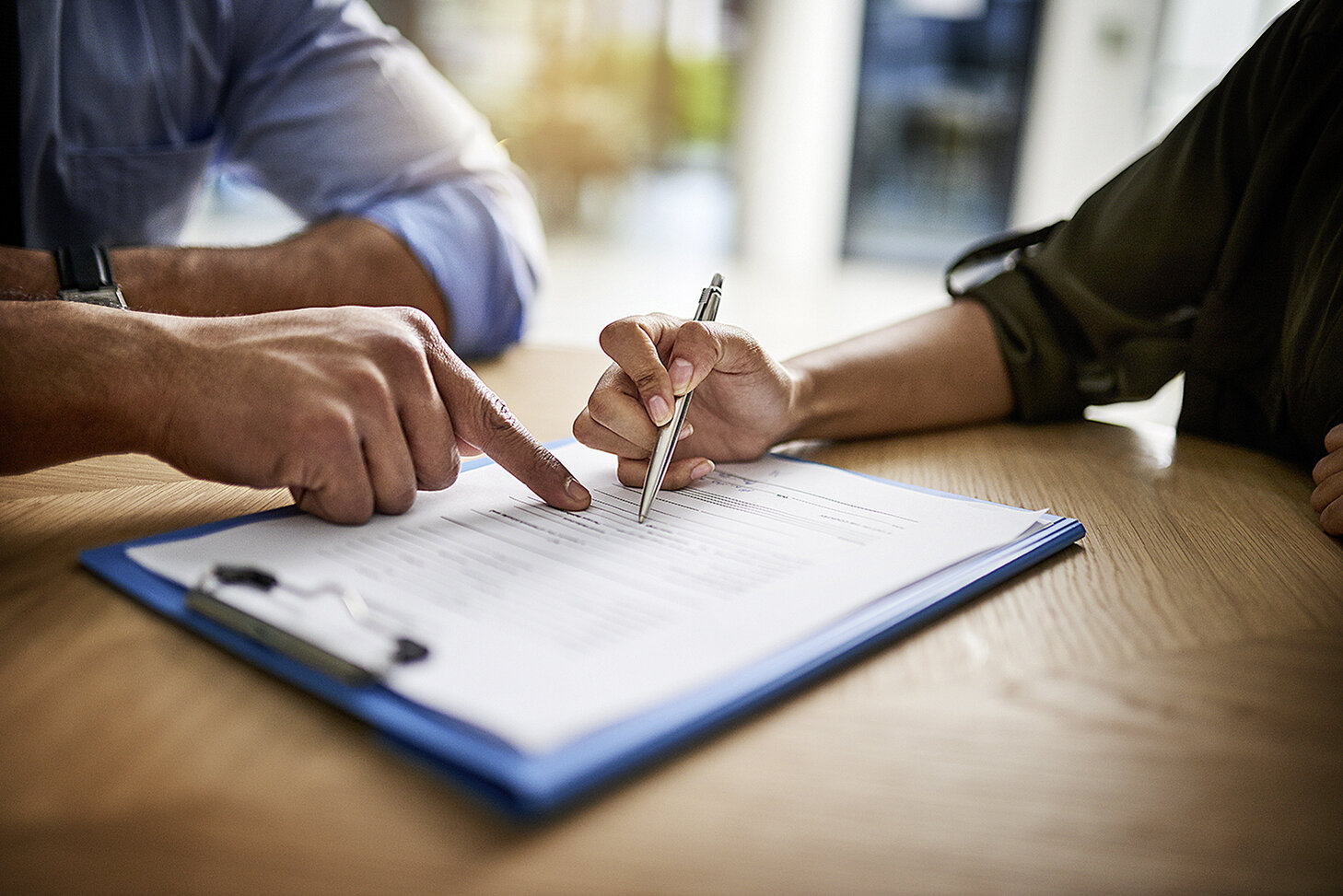 Ein Vertrag liegt auf dem Tisch, Hände von zwei Personen, die unterschreiben